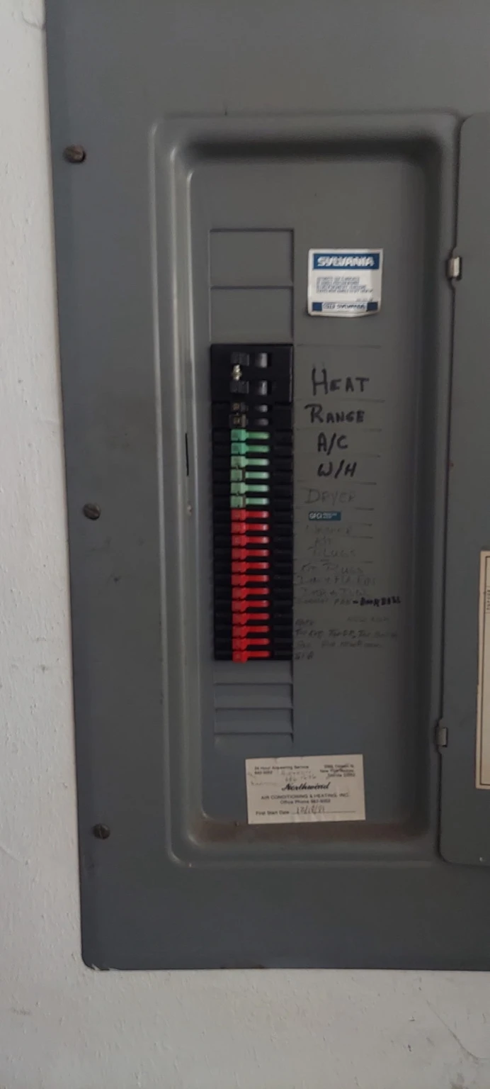 Older Sylvania-Zinsco electrical panel with its cover on, showing the green and red breakers and hand-written circuit labels