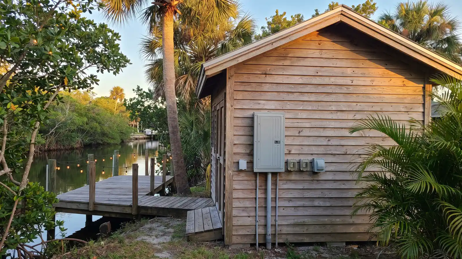 Backyard workshop with an exterior subpanel and a lit dock on a canal behind